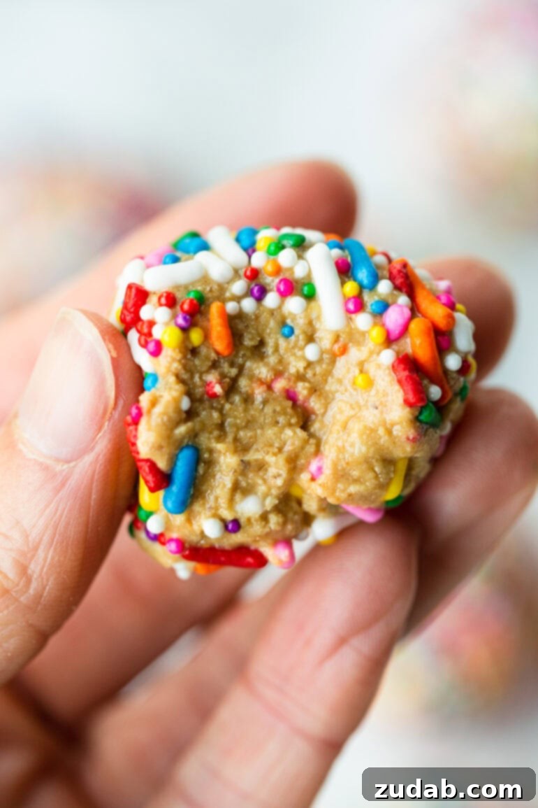 Funfetti Protein Poppers 5 a photo of someone holding a birthday cake protein ball that has a bite taken out of it