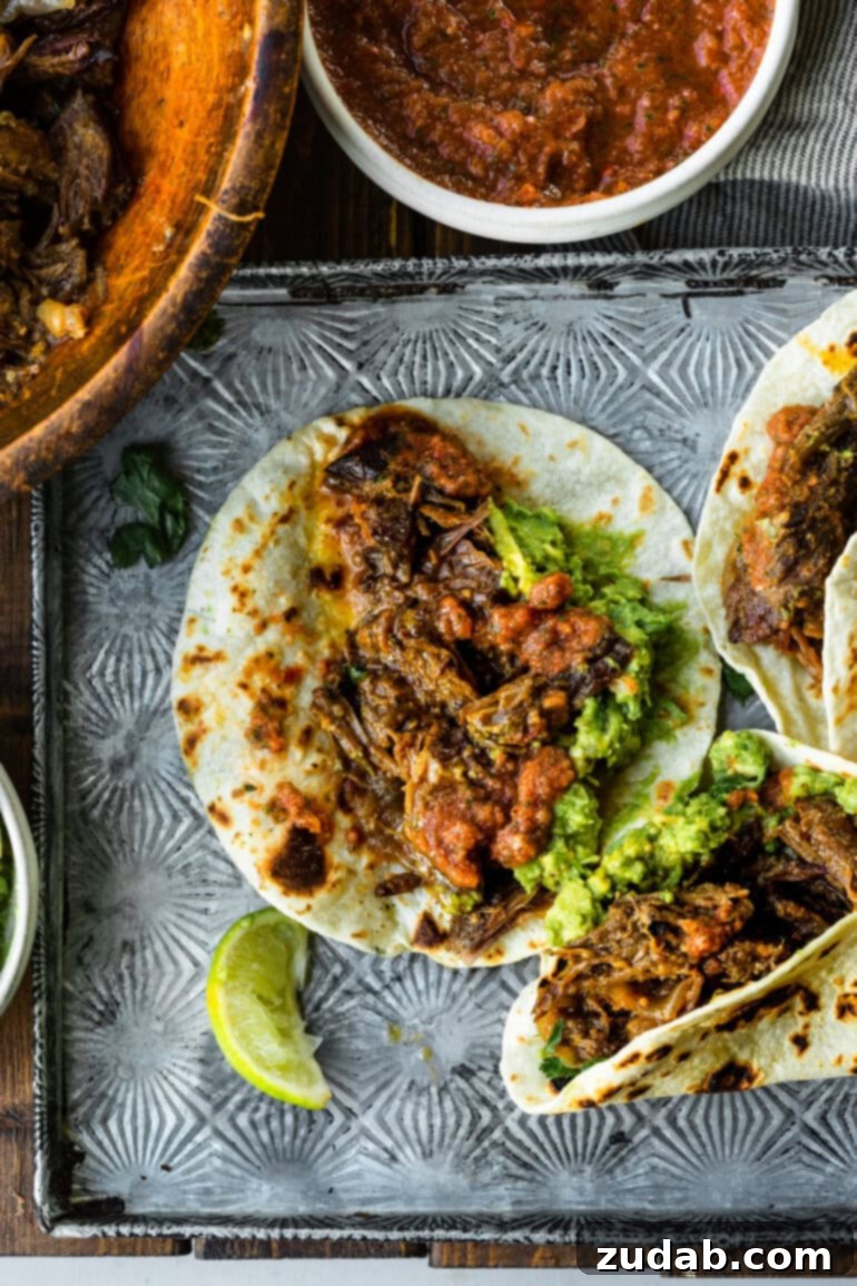 Deliciously Easy 5-Ingredient Shredded Beef Tacos 12 An enticing spread of several shredded beef tacos on flour tortillas, accompanied by a side of fresh guacamole, ready for a delightful meal.