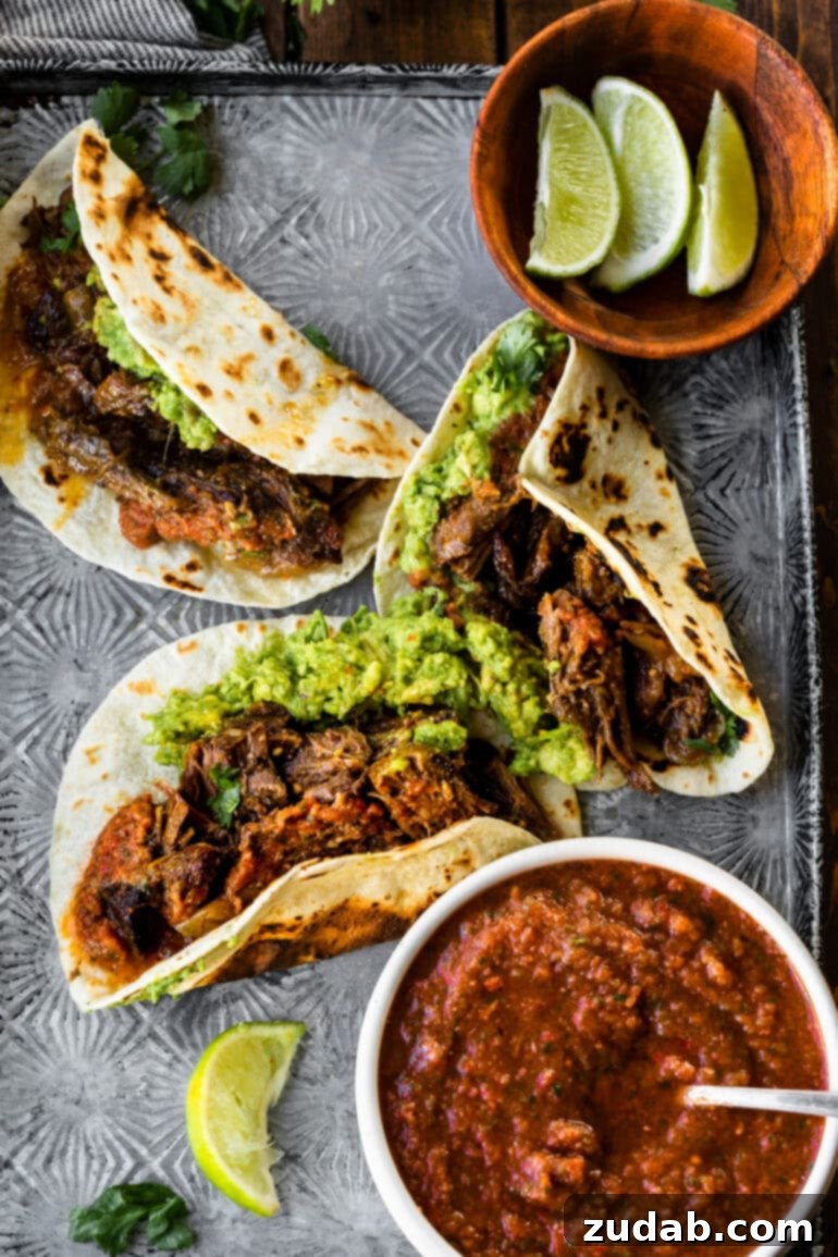 Deliciously Easy 5-Ingredient Shredded Beef Tacos 14 A baking sheet filled with several beautifully assembled shredded beef tacos on flour tortillas, accompanied by a bowl of fresh salsa and a scatter of lime wedges, ready to be devoured.