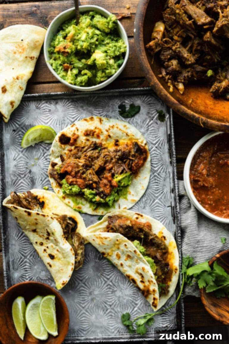 Deliciously Easy 5-Ingredient Shredded Beef Tacos 10 Several delectable shredded beef tacos on soft flour tortillas, artfully arranged next to a bowl of vibrant green guacamole, inviting you to dig in.