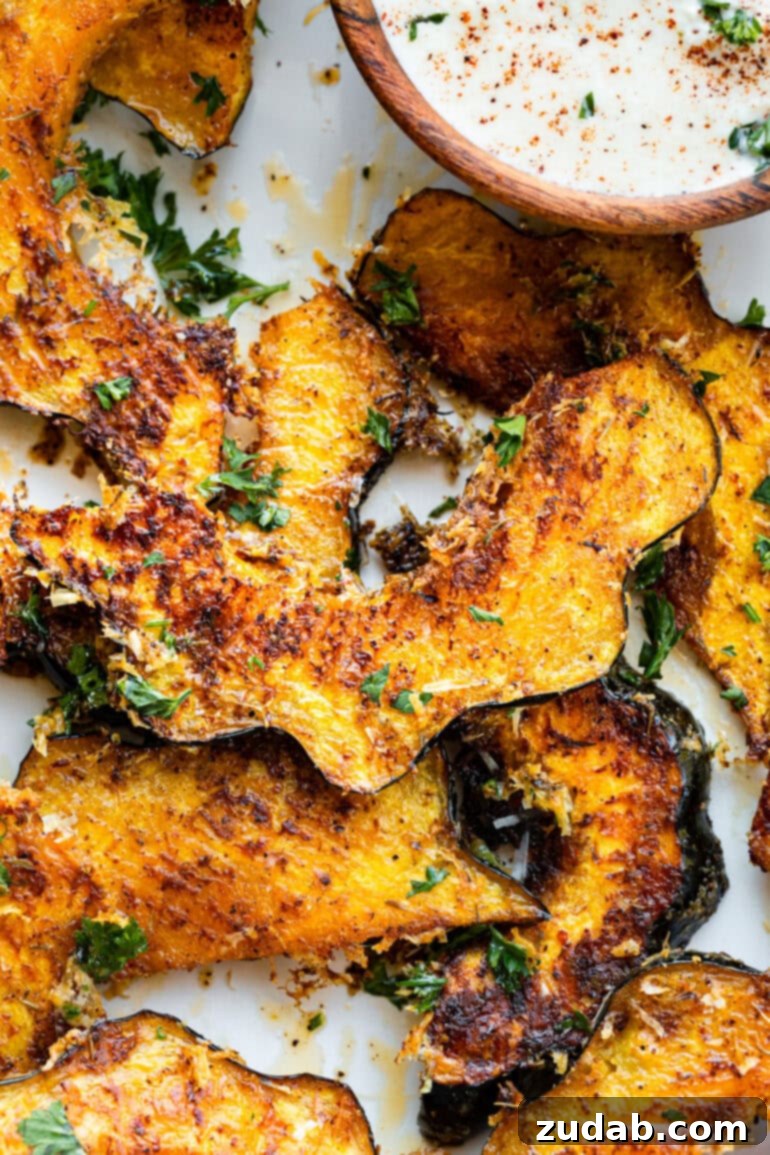 Golden Herb-Cheese Acorn Roast 2 A photo of several golden-brown slices of roasted acorn squash, adorned with crispy Parmesan cheese and fresh green parsley, ready to be served.