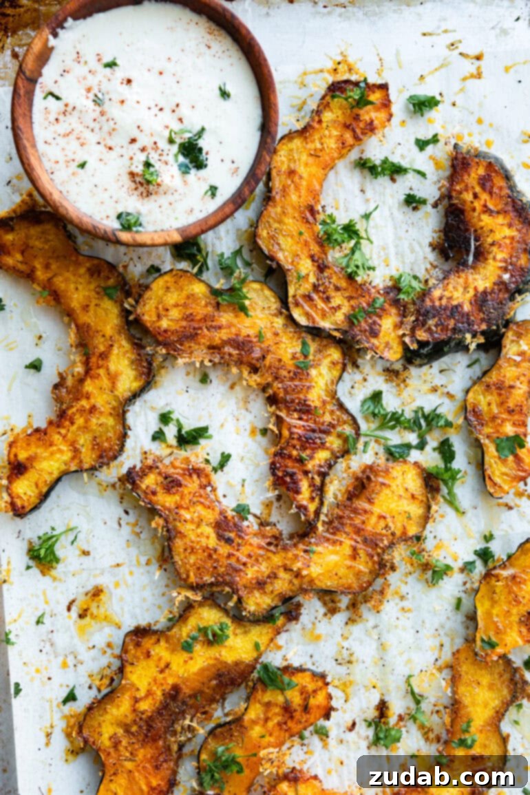 Golden Herb-Cheese Acorn Roast 4 A photo showcasing several beautifully roasted acorn squash slices, topped with golden crispy cheese and aromatic herbs, with a small, creamy dip nestled beside them, perfect for a cozy meal.