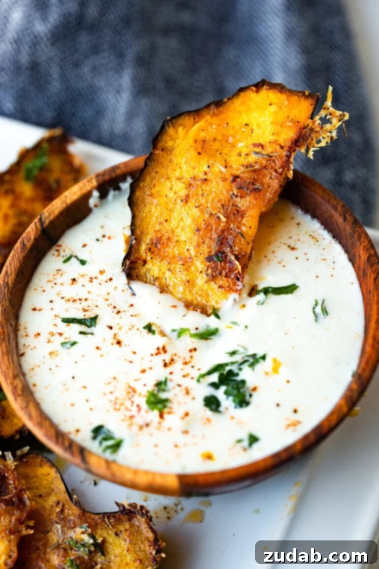 Golden Herb-Cheese Acorn Roast 6 A single, perfectly roasted acorn squash slice, glistening with crispy cheese and herbs, poised for dipping into a small, inviting bowl of creamy sauce, highlighting its irresistible appeal.