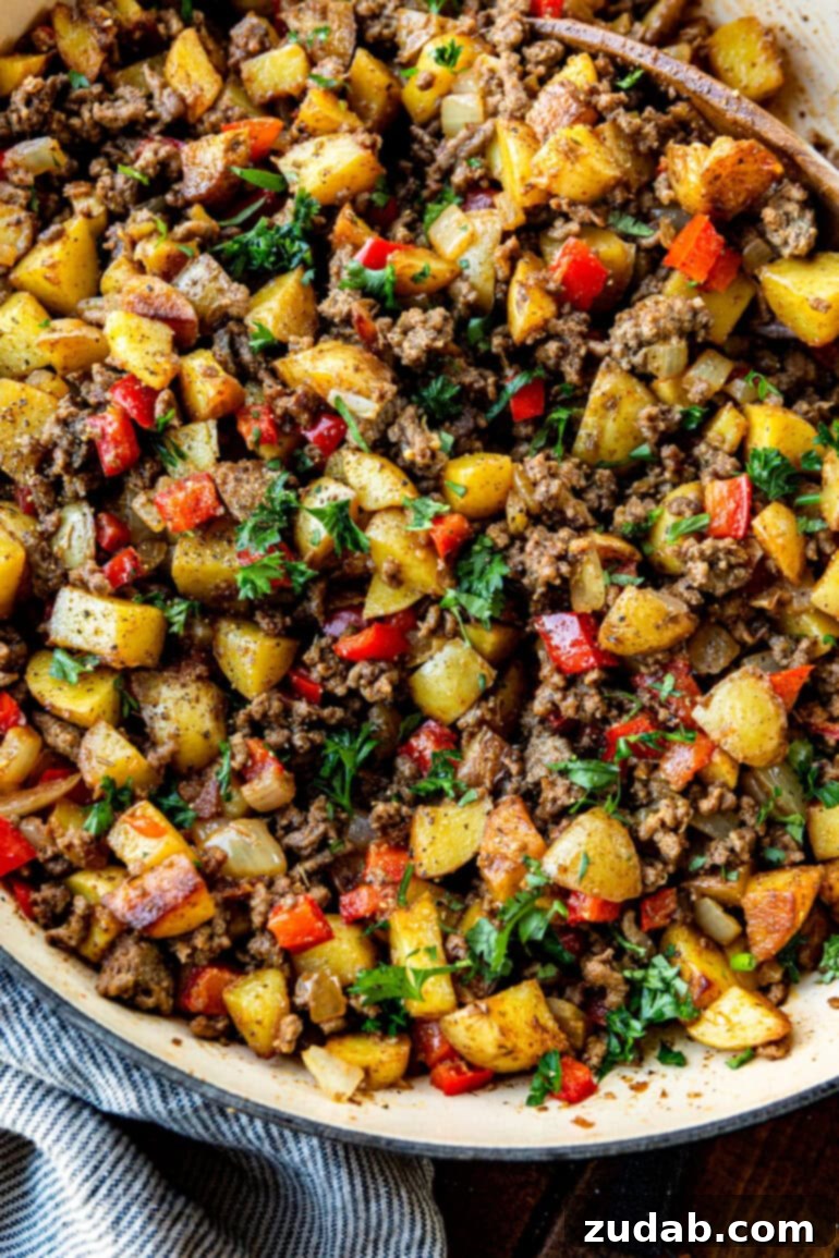 Quick & Hearty Beef and Potato Skillet 2 A vibrant photo of a cast iron skillet filled with golden brown crispy potatoes, seasoned ground beef, sautéed onions, and red bell peppers, garnished with fresh parsley, ready to serve as a hearty meal.