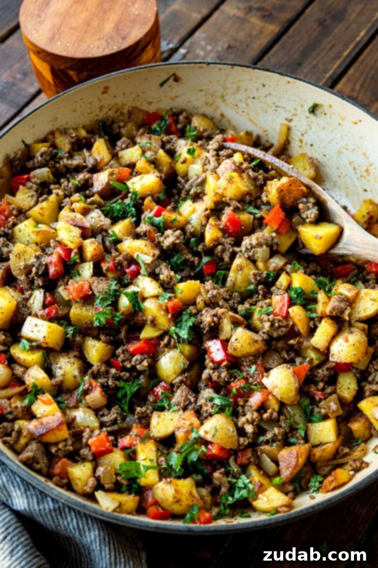 Quick & Hearty Beef and Potato Skillet 4 A close-up photo of the finished ground beef and potatoes dish in a cast iron skillet, rich with cooked beef, tender potatoes, and colorful bell peppers, generously topped with fresh green parsley.