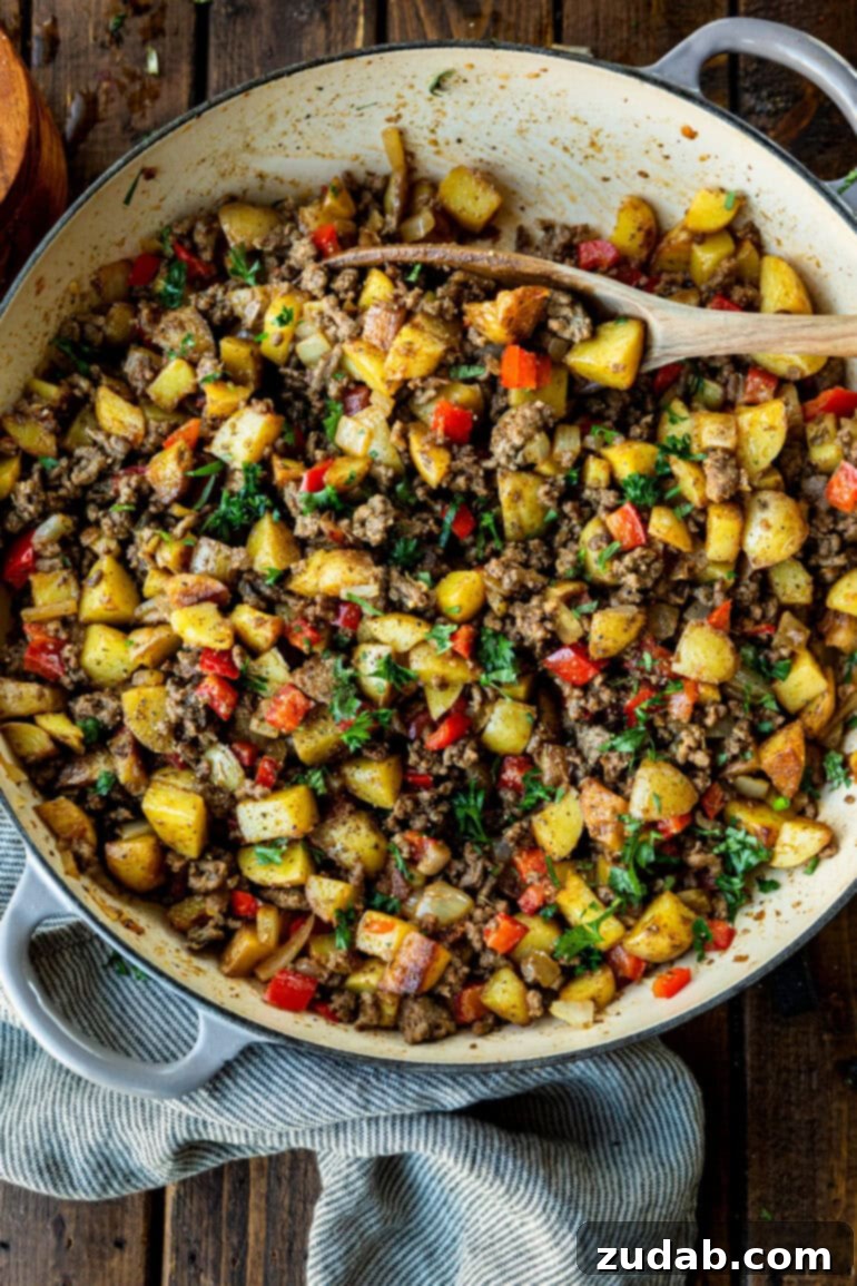 Quick & Hearty Beef and Potato Skillet 5 A top-down view of crispy potatoes, cooked ground beef, diced onions, and red bell peppers, beautifully arranged and garnished with fresh parsley in a large cast iron skillet, highlighting the dish's comforting appeal.