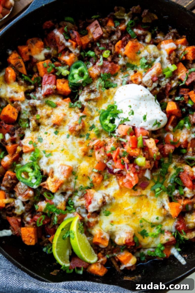 Taco Beef and Sweet Potato Skillet 2 A close-up photo of a cast iron skillet brimming with seasoned taco ground beef and perfectly diced sweet potatoes, generously topped with a dollop of cool sour cream, a sprinkle of fresh chopped cilantro, and bright lime wedges ready to be squeezed. This vibrant dish makes a quick and easy, healthy one-pan meal for busy weeknights.