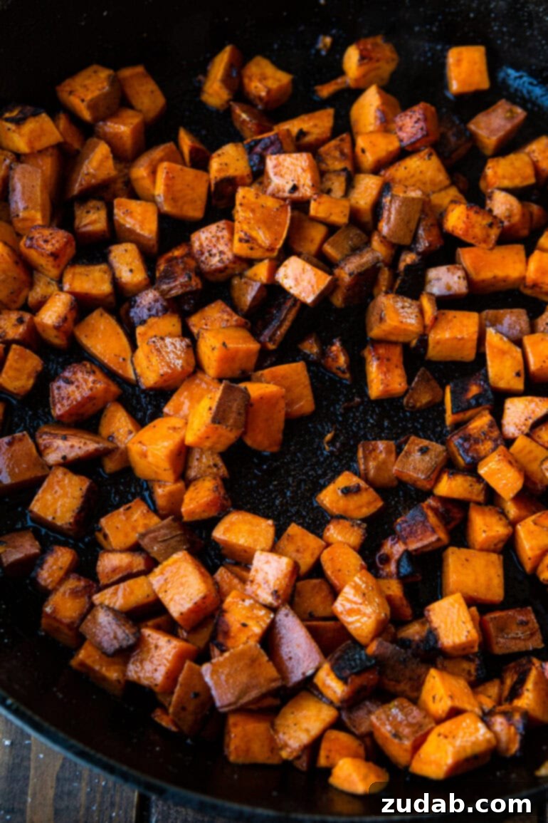 Taco Beef and Sweet Potato Skillet 4 A close-up photo of vibrant orange cubed sweet potatoes perfectly sautéed and slightly caramelized in a cast iron skillet, showcasing their readiness to be combined with the taco-seasoned ground beef. This image highlights the delicious texture and color achieved during the cooking process for a healthy and quick weeknight meal.
