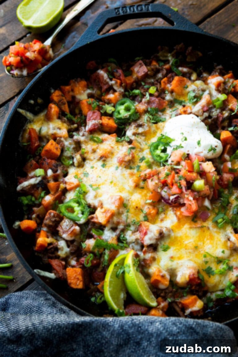 Taco Beef and Sweet Potato Skillet 6 A vibrant overhead shot of a cast iron skillet filled with delicious ground beef taco and sweet potato hash, garnished with fresh cilantro and a dollop of sour cream. This image captures the wholesome and satisfying nature of this one-pan meal, highlighting its appeal for a healthy weeknight dinner.