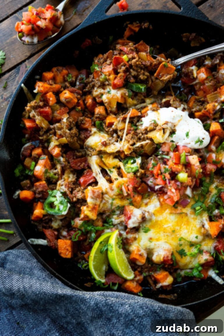 Taco Beef and Sweet Potato Skillet 7 A final, mouthwatering shot of a cast iron skillet overflowing with ground beef taco and sweet potato deliciousness, beautifully garnished with cool sour cream, bright lime wedges, finely diced purple onions, and vibrant sliced jalapeños. This image epitomizes the quick, easy, and flavorful nature of this one-pan, healthy weeknight meal.
