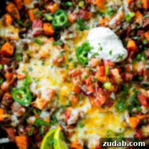 Taco Beef and Sweet Potato Skillet 8 a photo of a cast iron skillet full of taco ground beef and diced sweet potatoes topped with a dollop of sour cream, chopped fresh cilantro and lime wedges