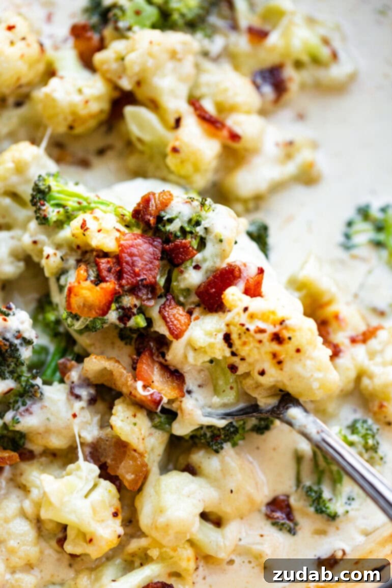 Creamy Garlic Parmesan Broccoli Cauliflower with Crispy Bacon 2 A close-up photo of a serving spoon lifting a generous portion of creamy garlic parmesan broccoli and cauliflower, glistening with sauce and topped with crispy bacon bits. The background shows a rustic table setting, emphasizing its appeal as a comforting side dish.