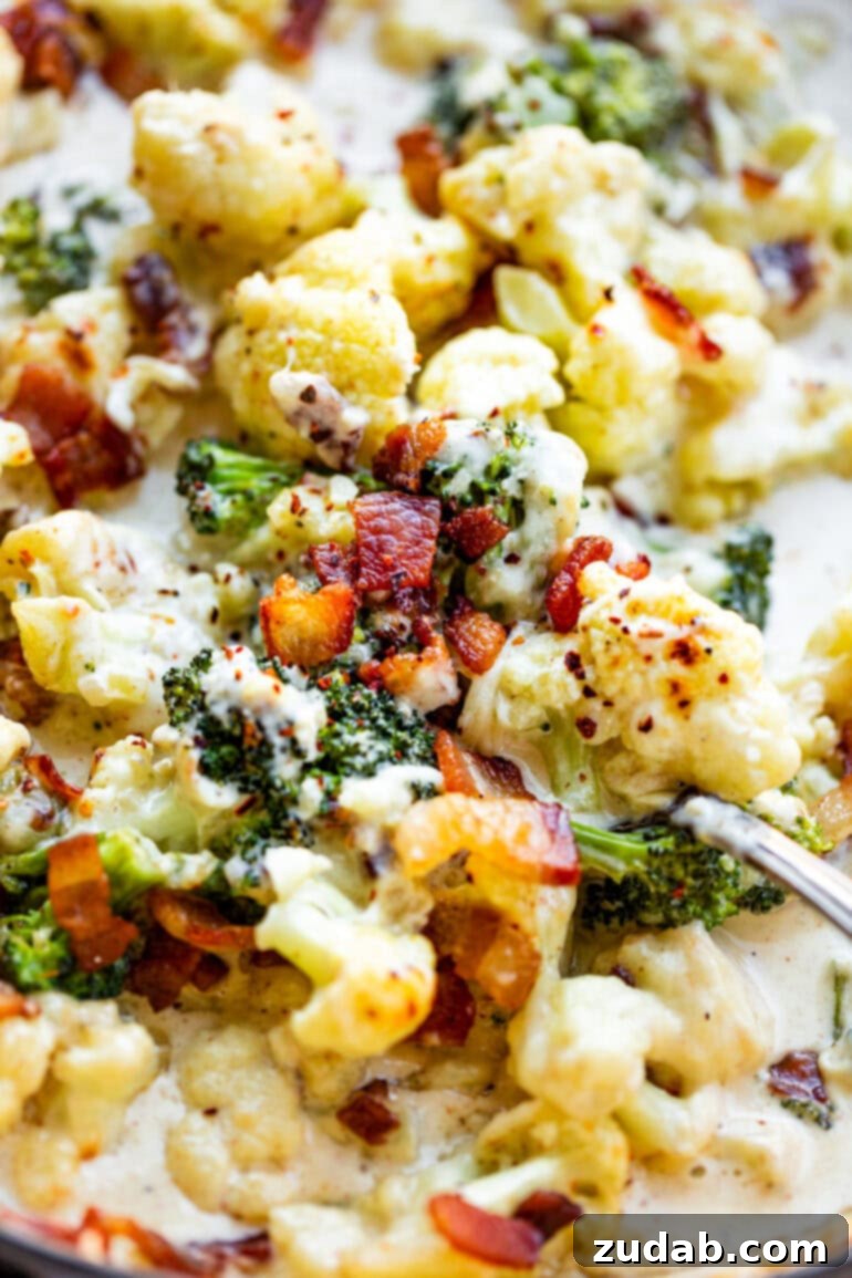 Creamy Garlic Parmesan Broccoli Cauliflower with Crispy Bacon 11 A hand scooping a generous portion of creamy garlic parmesan broccoli and cauliflower from a skillet, emphasizing its delicious appeal and readiness to be served.