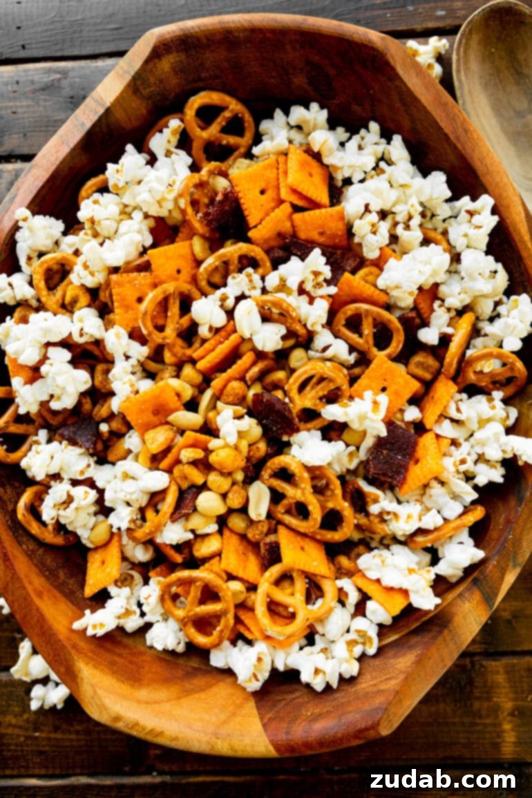 Super Bowl's Ultimate Manly Snack Attack 4 A beautifully composed shot of a large, rustic wooden bowl filled to the brim with a rich, hearty popcorn snack mix. It prominently features a diverse array of textures and colors from pretzels, Cheez-It crackers, roasted peanuts, savory beef jerky, and crunchy corn nuts, making it visually appealing and mouth-watering.