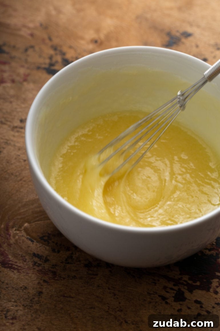 A bowl of white chocolate butter sauce ingredients being whisked together, creating a smooth and creamy consistency.