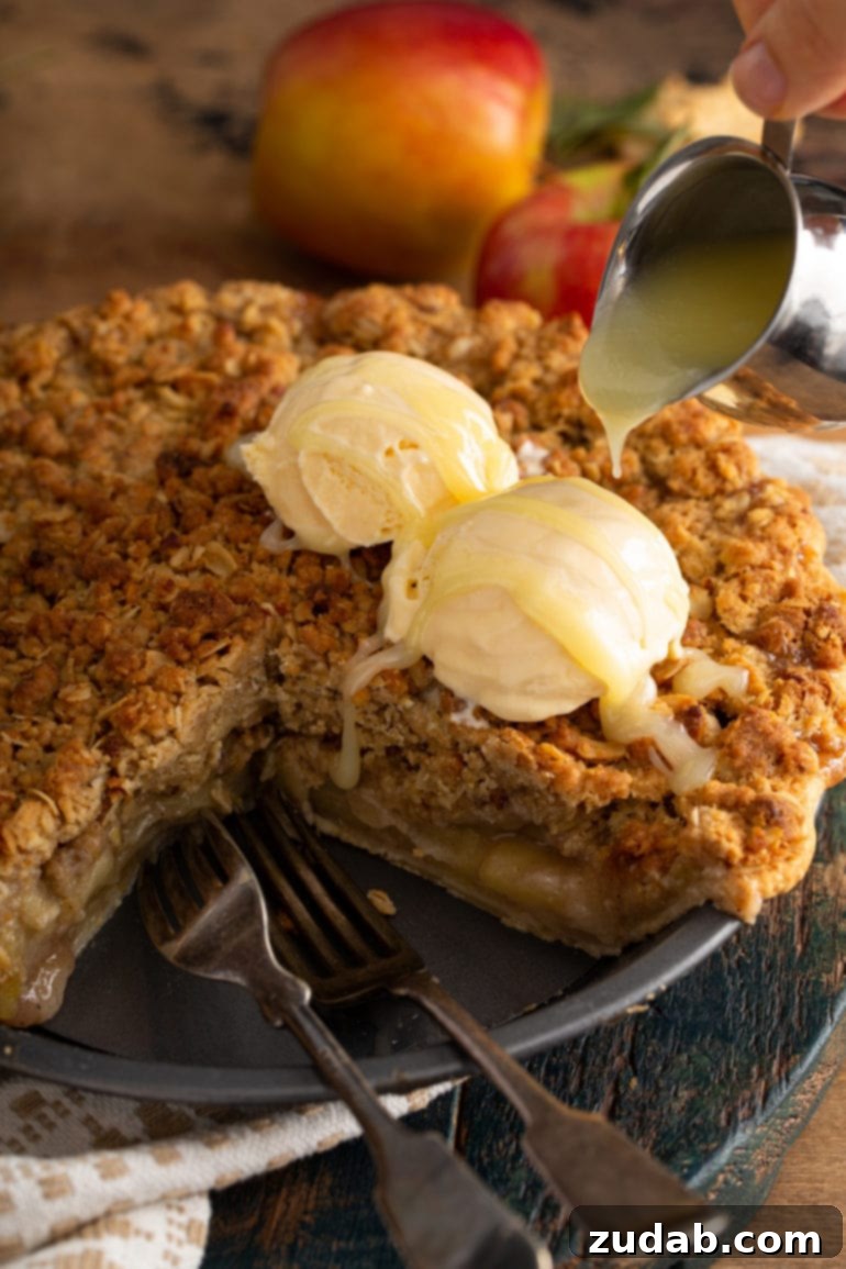 A Dutch apple pie with a slice removed, revealing two scoops of vanilla ice cream melting on top, generously adorned with a rich white chocolate butter sauce.
