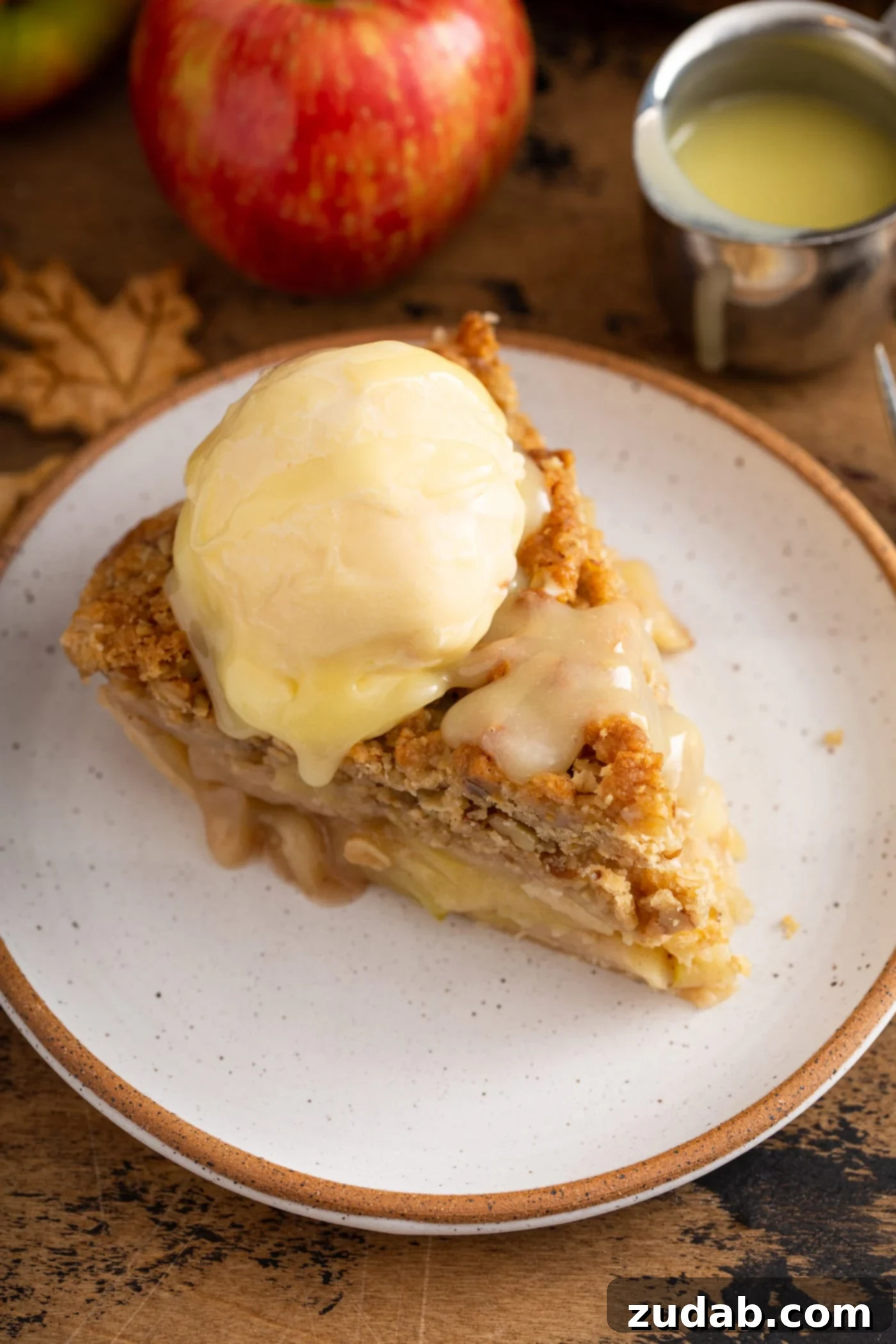 A tempting slice of Dutch apple pie, crowned with a scoop of vanilla ice cream and generously drizzled with the luxurious white chocolate butter sauce, inviting a taste.