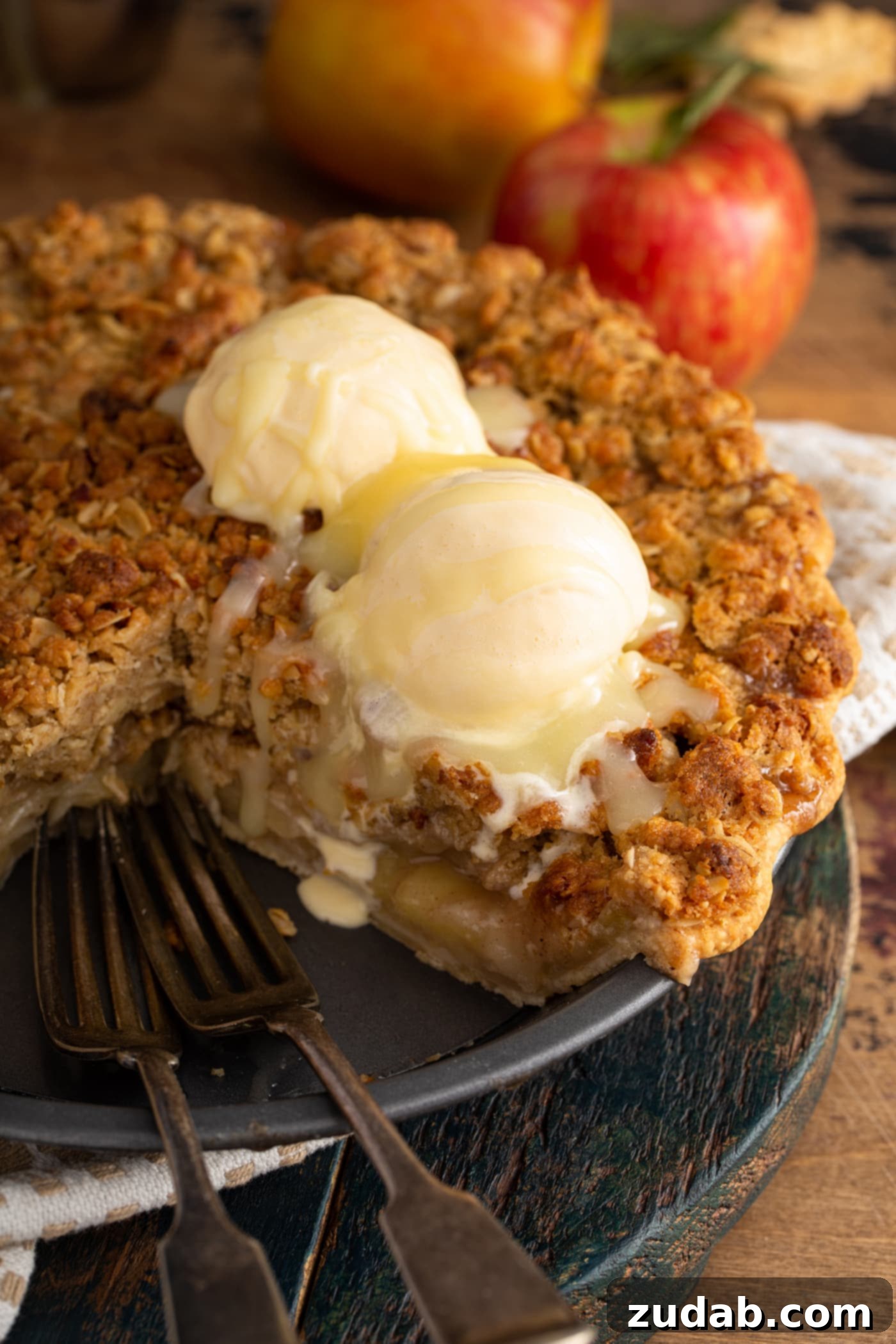 A whole Dutch apple pie with a slice removed, adorned with two scoops of vanilla ice cream melting into the warm pie, all elegantly drizzled with the signature white chocolate butter sauce.