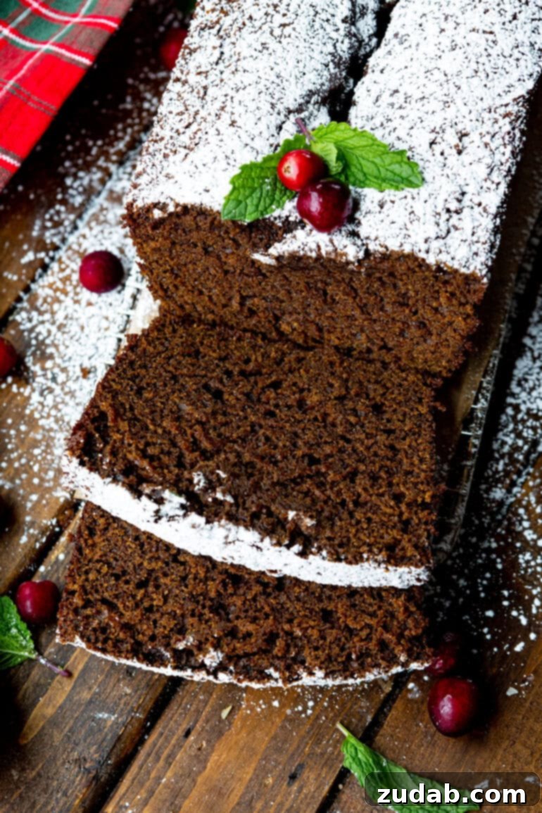 Warm Spiced Gingerbread Loaf 14 A loaf of gingerbread with several slices cut, topped with powdered sugar, two whole cranberries, and greenery.