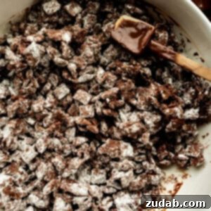 dark chocolate coated chex cereal being stirred in a white mixing bowl with a rubber spatula