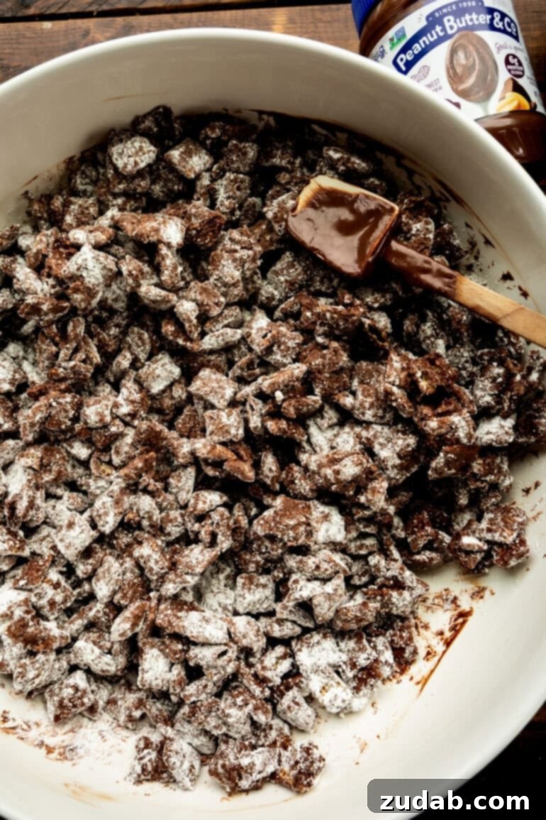 Decadent Dark Chocolate Peanut Butter Muddy Buddies 8 dark chocolate coated chex cereal being stirred in a white mixing bowl with a rubber spatula