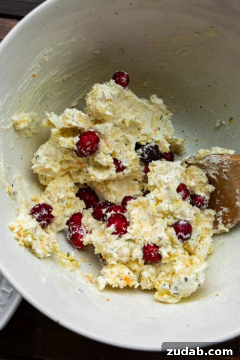 Baked Cranberry Bliss Dip 6 A close-up shot of cream cheese, vibrant whole cranberries, and grated cheese being mixed together in a white bowl with a wooden spoon, illustrating the preparation process.