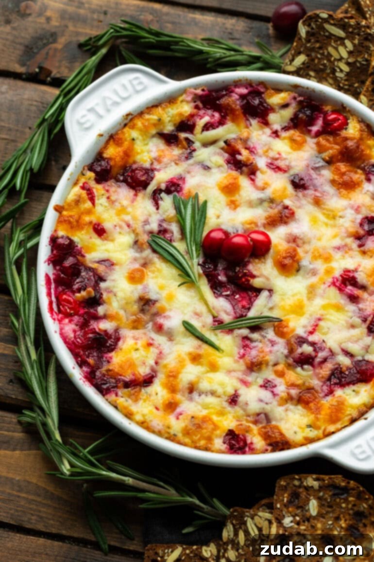 Baked Cranberry Bliss Dip 8 A delicious cheesy cranberry cream cheese dip in a circular cast iron baking dish, elegantly topped with fresh rosemary and whole cranberries.