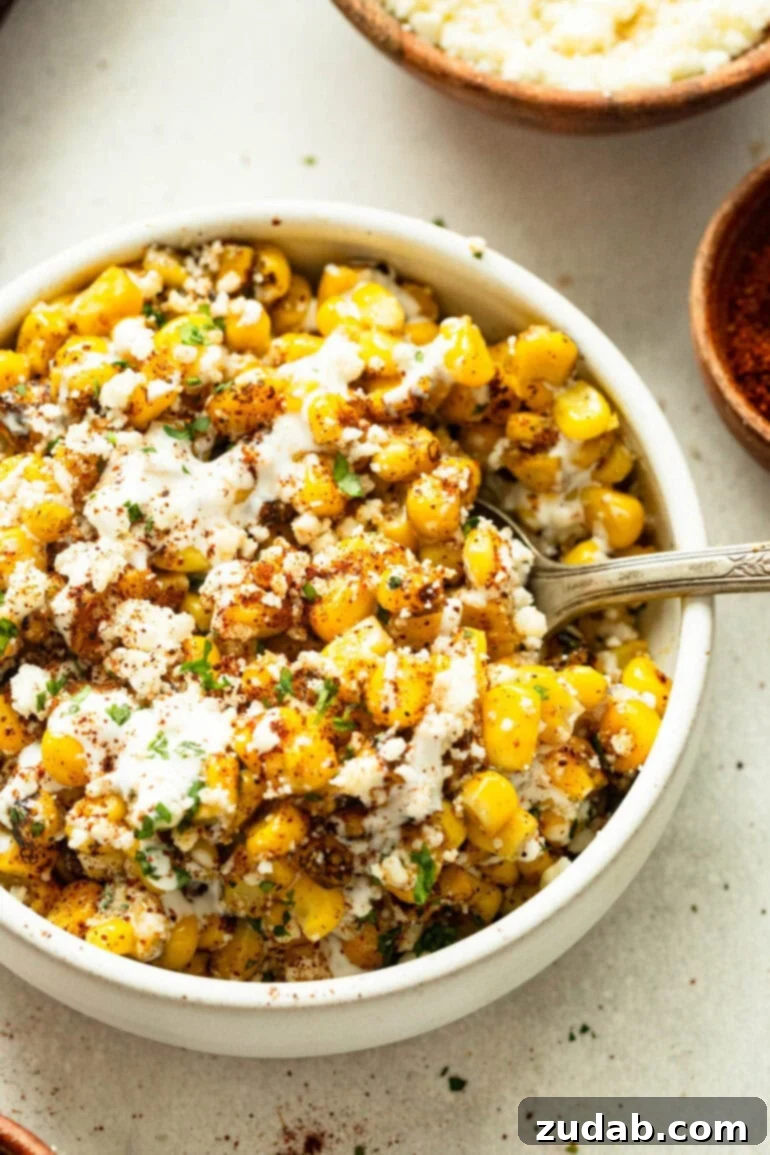 Oven Baked Sheet Pan Mexican Street Corn 2 A beautifully presented serving bowl full of roasted sheet pan Mexican street corn, generously topped with crumbled cotija cheese and a sprinkle of chili powder.