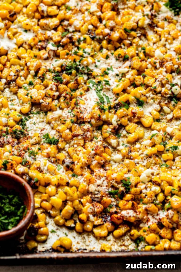 Oven Baked Sheet Pan Mexican Street Corn 5 A baking sheet featuring roasted corn perfectly mixed with Mexican crema, chili powder, crumbled cotija cheese, and fresh cilantro, spread out and glistening.