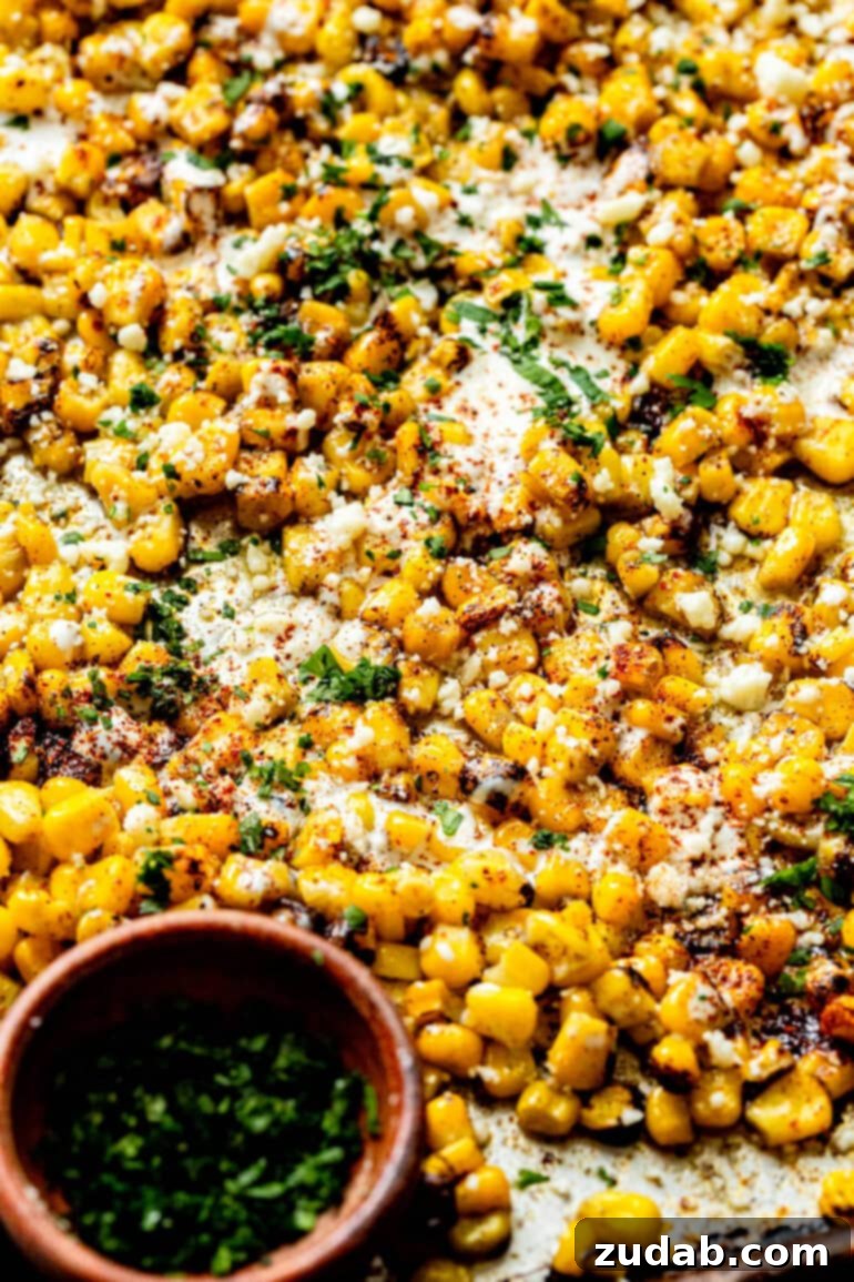 Oven Baked Sheet Pan Mexican Street Corn 8 An overhead shot of a sheet pan generously filled with roasted corn, beautifully mixed with cotija cheese, creamy Mexican crema, chili powder, and fresh cilantro, highlighting its vibrant textures.