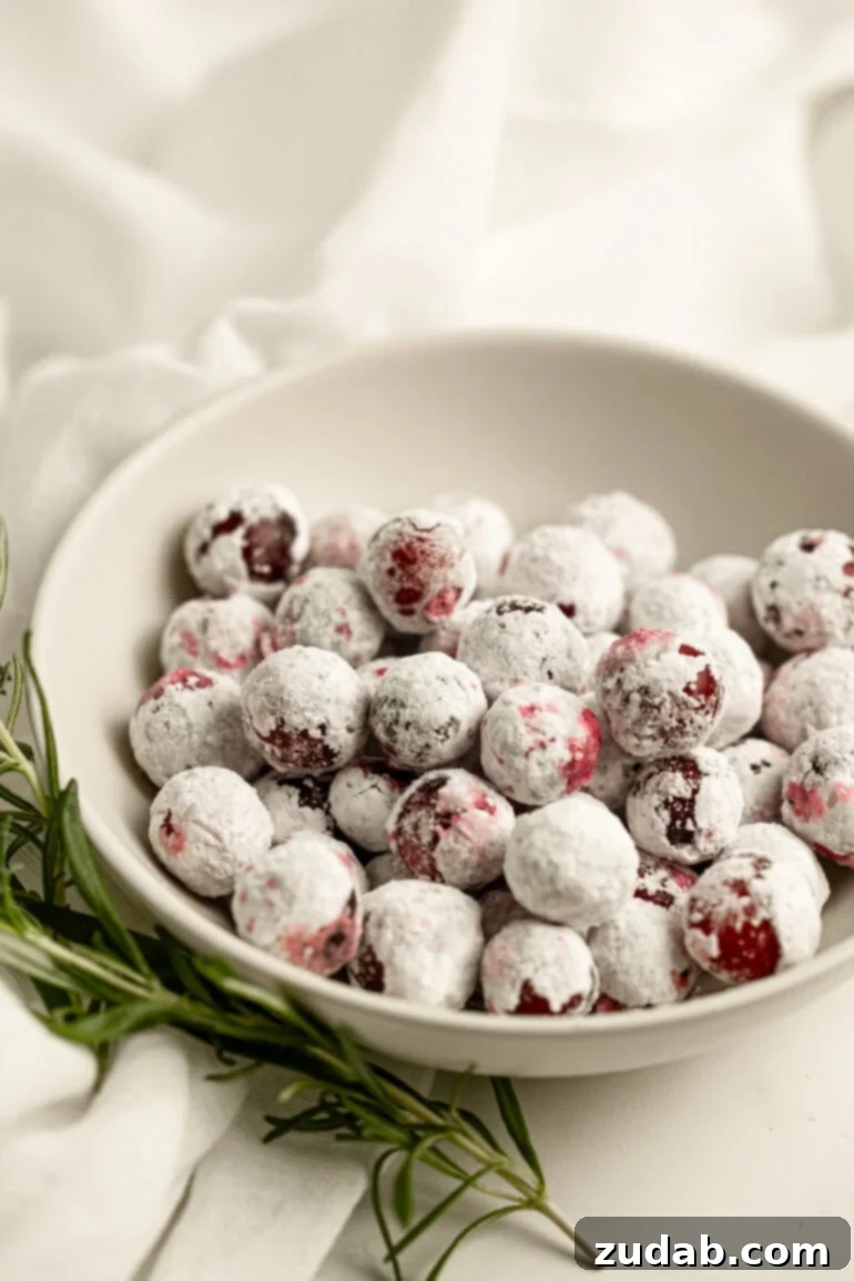 Sparkling Sweet Tart Cranberry Craze 2 A small bowl of sugar-coated whole cranberries with a sprig of fresh rosemary laying next to it, set against a festive backdrop. These sparkling sugared cranberries are a holiday hit!