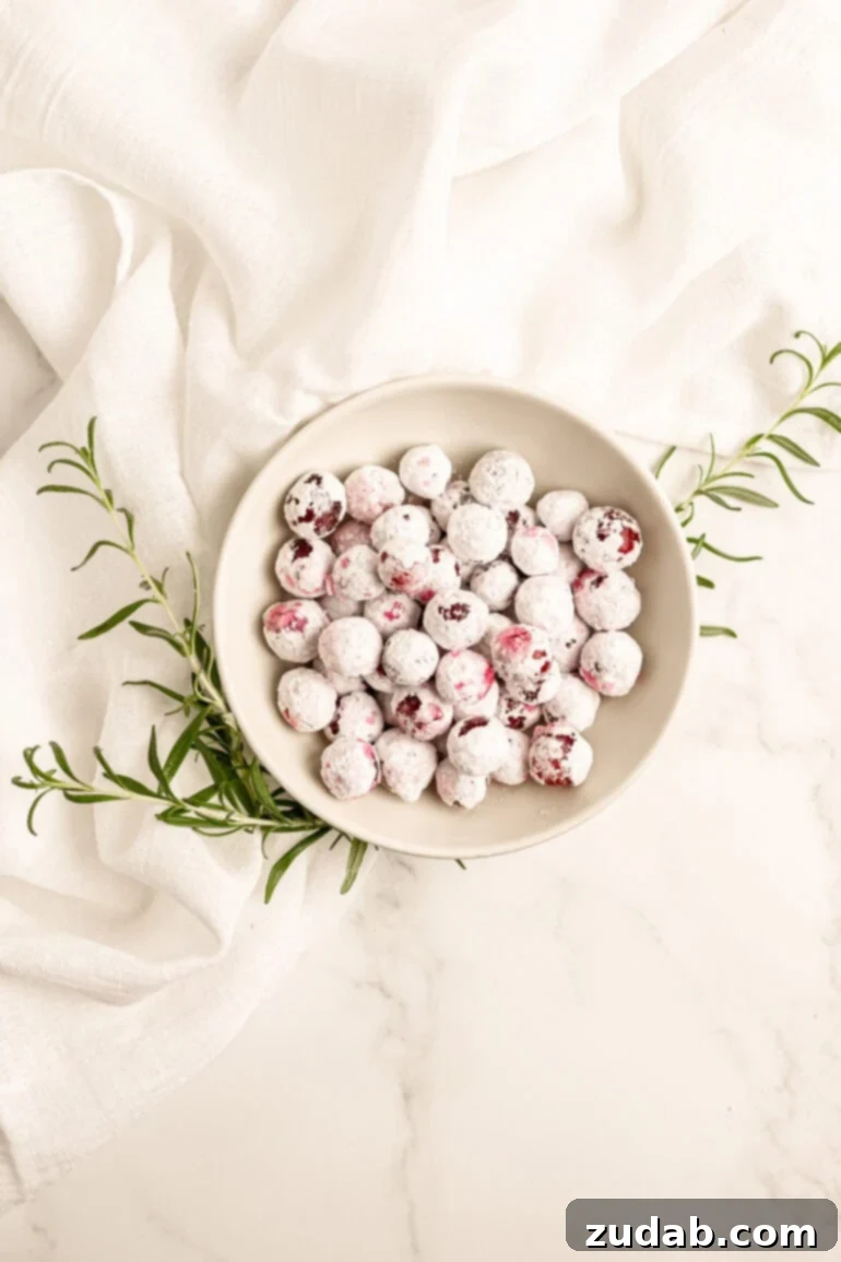 Sparkling Sweet Tart Cranberry Craze 9 A small bowl full of sparkling candied cranberries with sprigs of fresh rosemary sticking out from under the bowl, all on a white tablecloth. A perfect festive holiday treat.