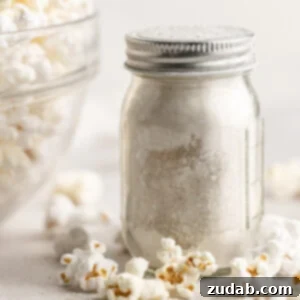 A small glass shaker jar full of caramel popcorn seasoning sitting next to a large glass bowl full of popped popcorn.