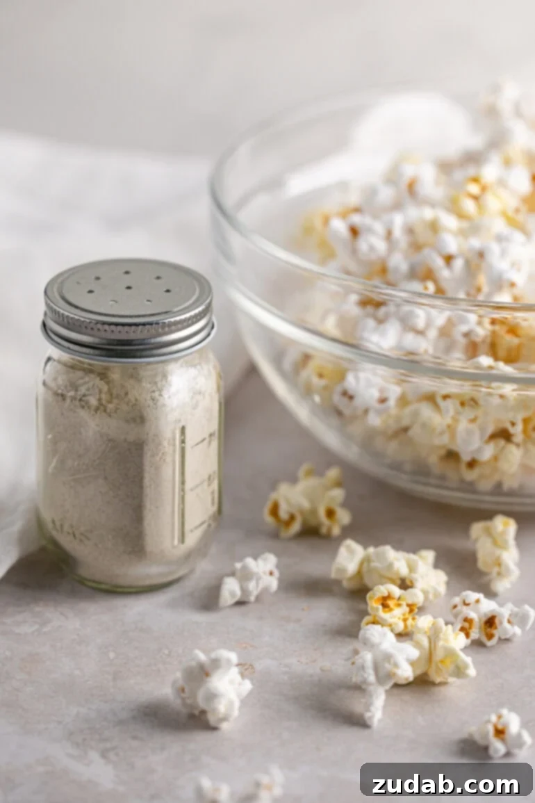 Signature Caramel Popcorn Blend 3 A glass shaker jar of homemade popcorn seasoning sitting next to a glass bowl of popped popcorn.