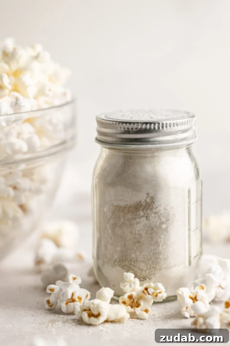 Signature Caramel Popcorn Blend 8 A small glass shaker jar full of caramel popcorn seasoning sitting next to a large glass bowl full of popped popcorn.