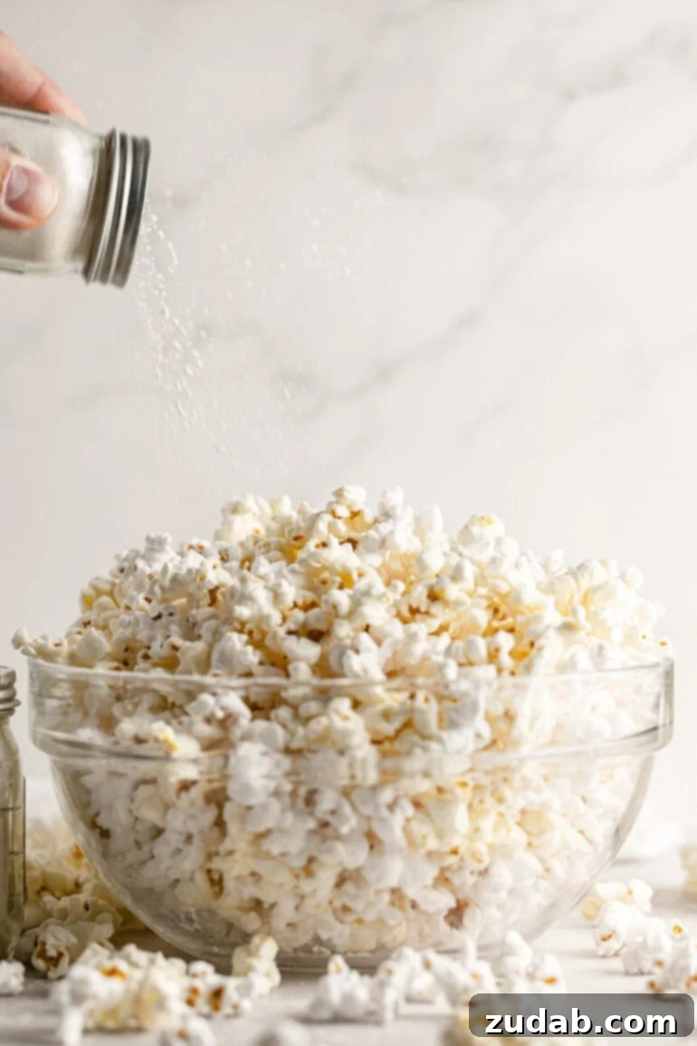 Signature Caramel Popcorn Blend 10 Caramel popcorn seasoning being shaken from a glass shaker bottle over the top of a bowl full of popped popcorn.
