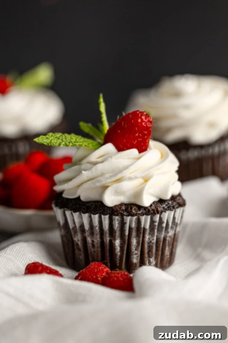 Light and Fluffy Cream Cheese Frosting 11 A delectable chocolate cupcake, nestled in its liner, topped with a generous swirl of piped cream cheese frosting, garnished with a single fresh raspberry and a couple of vibrant mint leaves.