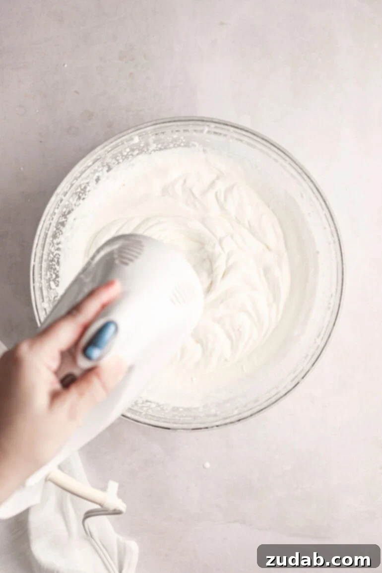Light and Fluffy Cream Cheese Frosting 4 Step-by-step image showing whipping cream being beaten to stiff peaks in a mixing bowl.