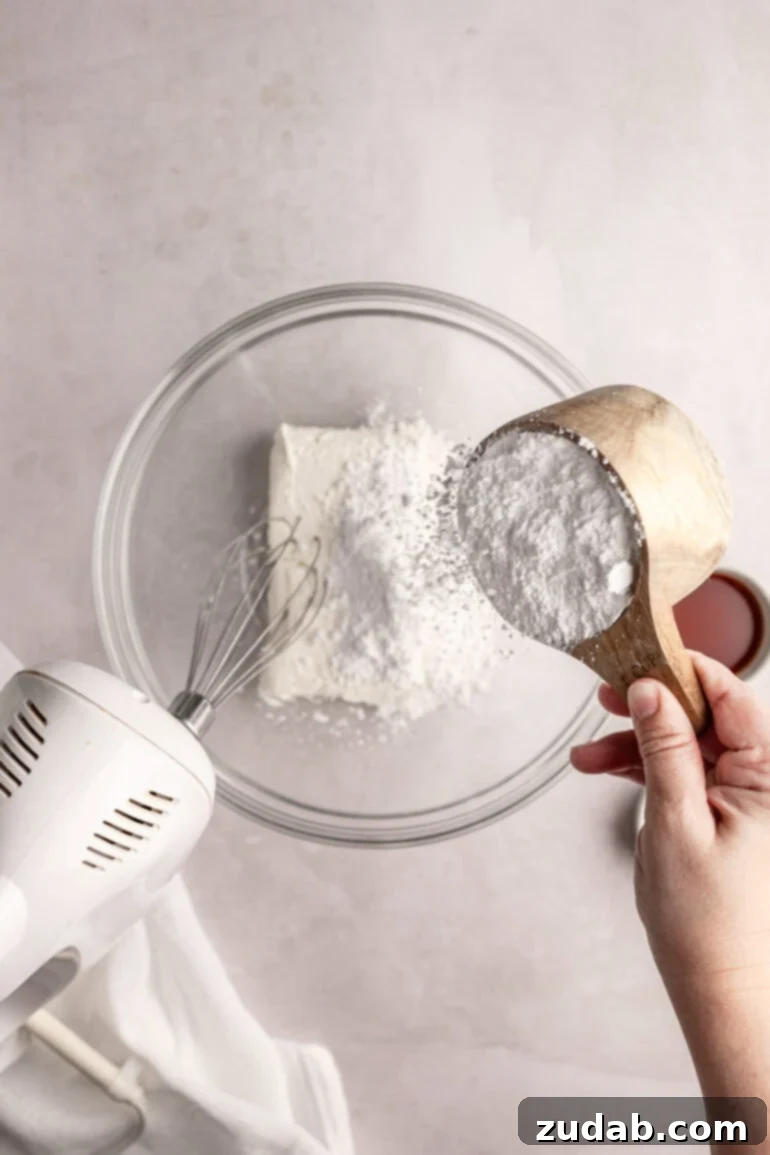 Light and Fluffy Cream Cheese Frosting 5 Step-by-step image showing cream cheese, powdered sugar, salt, and vanilla extract in a separate mixing bowl before mixing.