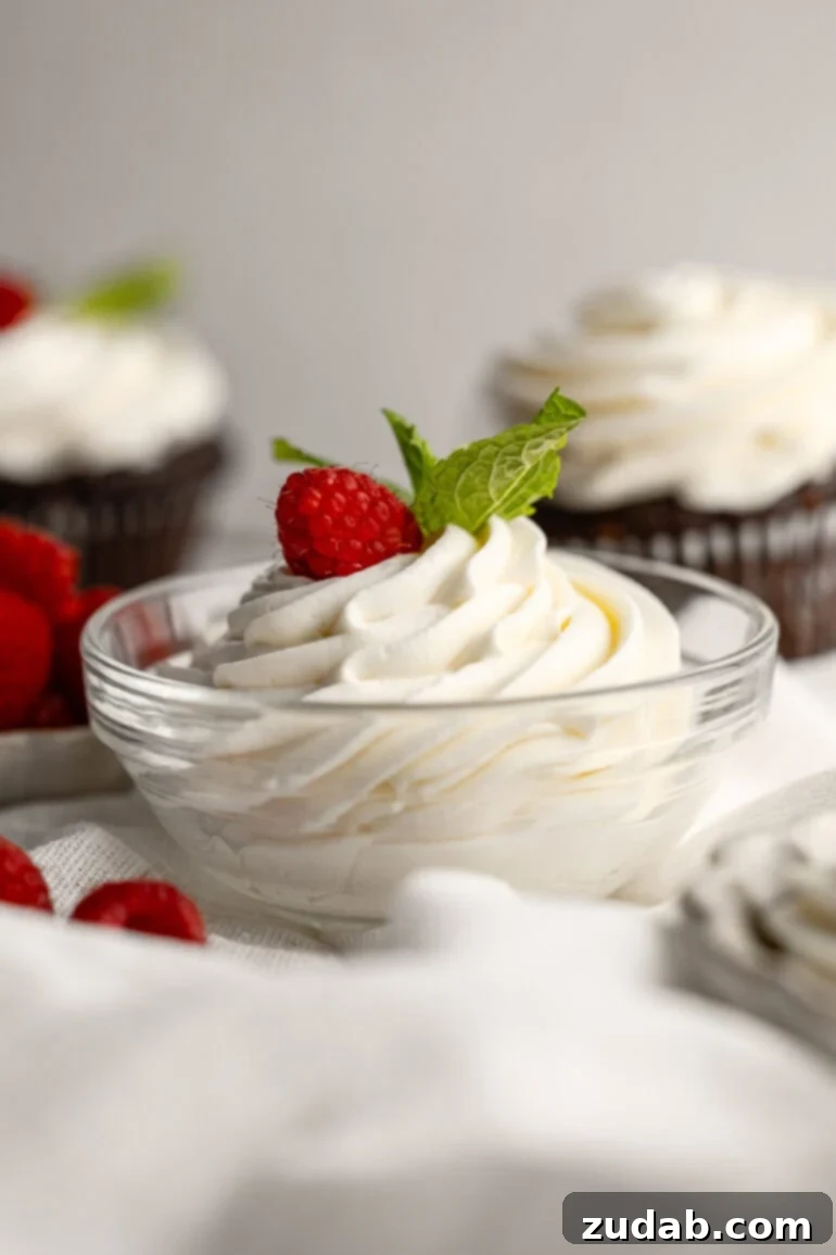 Light and Fluffy Cream Cheese Frosting 10 A small glass bowl brimming with beautifully piped whipped cream cream cheese frosting, adorned with a fresh raspberry and delicate mint leaves.