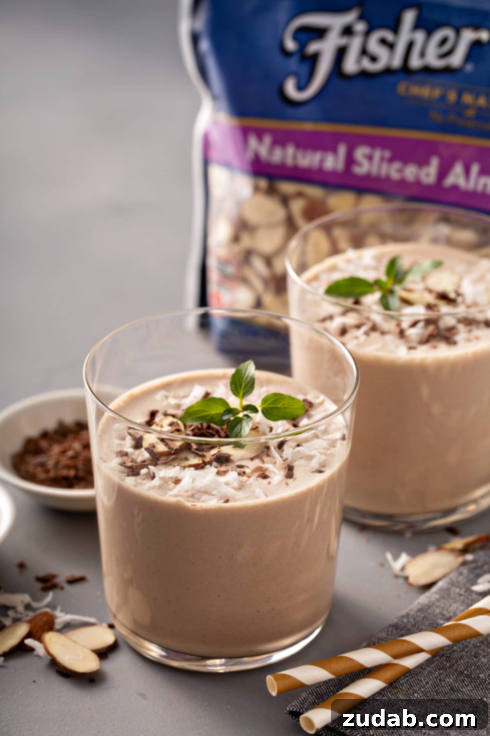 Two glasses of almond joy protein shakes, shaved chocolate, a package of Fisher's slivered almonds, coconut topped with mint leaves