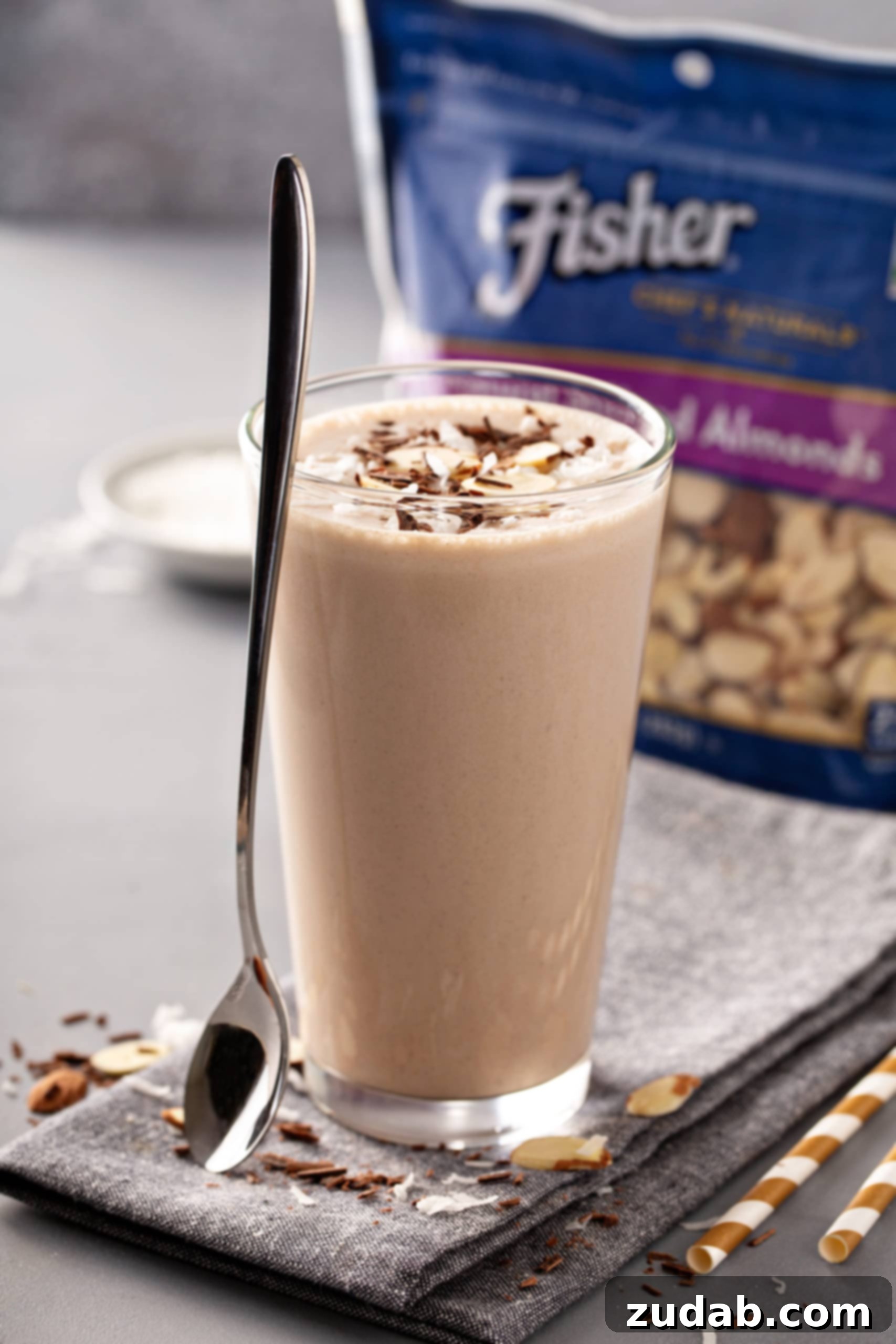 Tall glass of Almond Joy Chocolate Protein Shake with sliced almonds on top and a package of Fisher's Sliced almonds in the background
