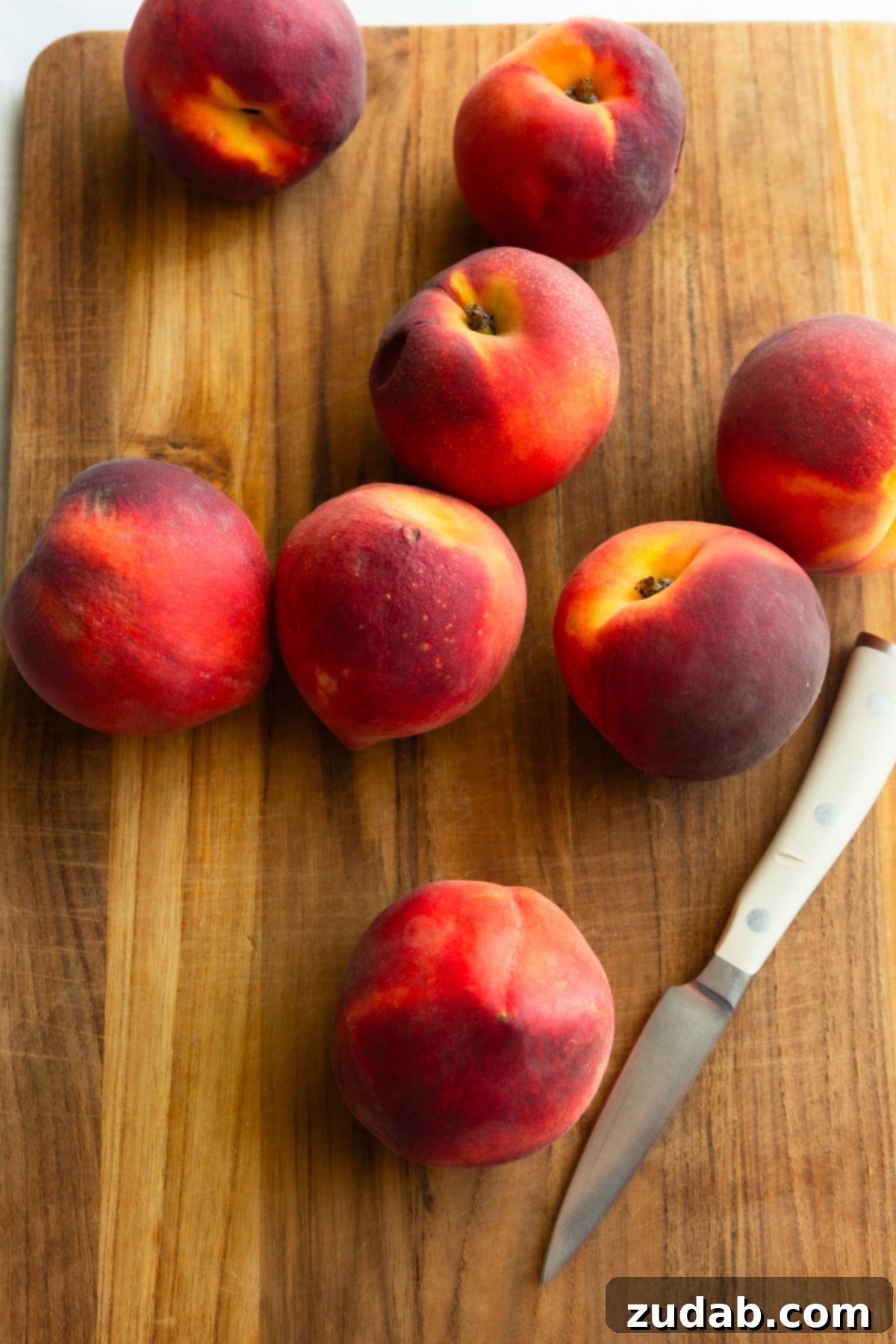 Freeze Peaches Perfectly Every Time 3 Whole ripe peaches resting on a wooden cutting board next to a paring knife.