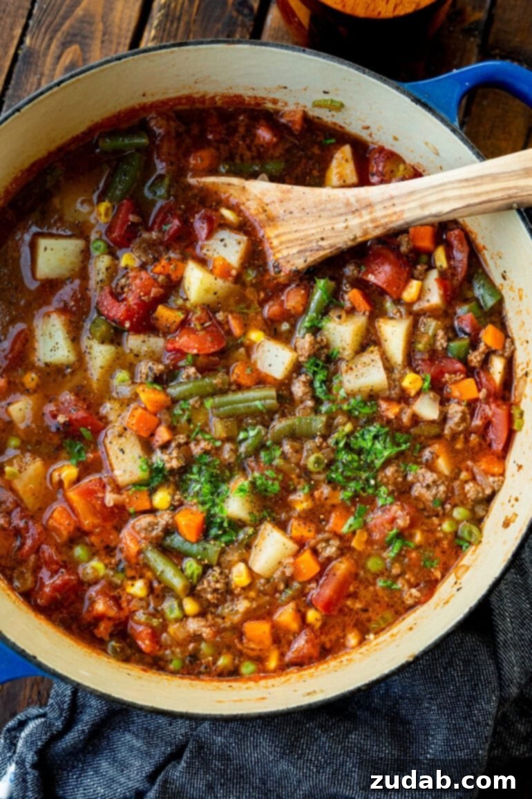 Quick and Easy Ground Beef Vegetable Soup 2 A large pot of ground beef vegetable soup, garnished with fresh minced parsley, with a wooden spoon resting in the bowl, ready to serve.