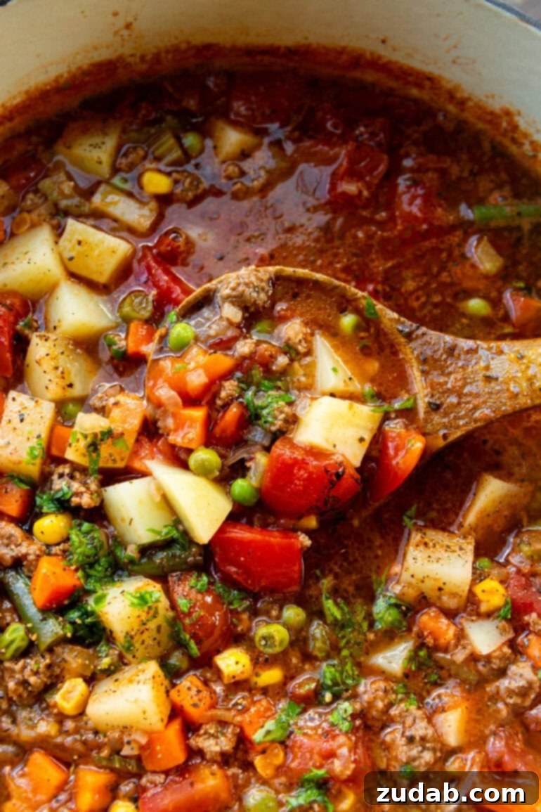 Quick and Easy Ground Beef Vegetable Soup 3 A wooden spoon lifting a spoonful of rich ground beef and vegetables from a steaming pot of hamburger soup, showcasing the hearty texture.