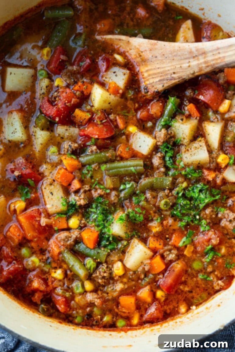 Quick and Easy Ground Beef Vegetable Soup 6 A wooden spoon stirring a pot of simmering ground beef vegetable soup, showing the rich color and abundance of ingredients.