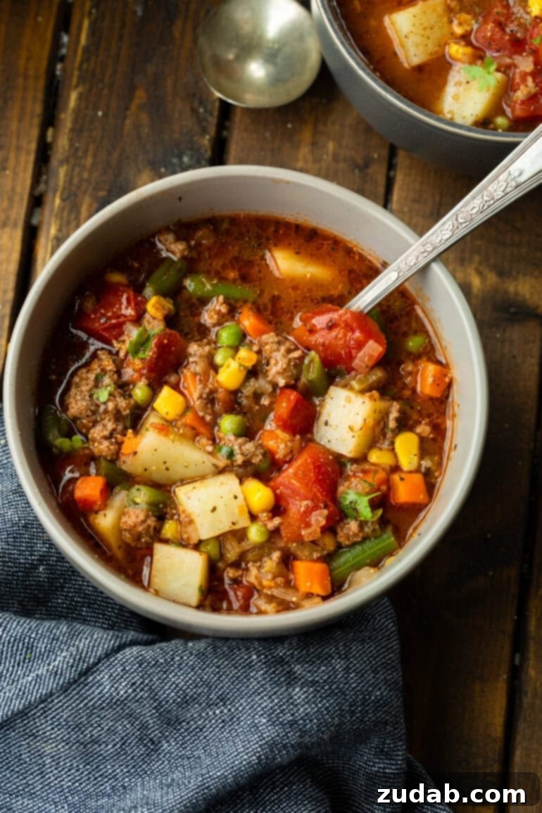 Quick and Easy Ground Beef Vegetable Soup 8 A cozy bowl full of ground beef vegetable soup, perfectly garnished with fresh parsley, with a spoon nestled within, inviting you to enjoy.