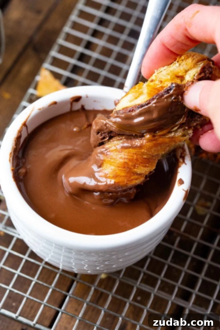 Festive Puff Pastry Tree 3 A close-up of a twisted puff pastry branch being dipped into a luscious pool of chocolate sauce, showcasing the irresistible pull-apart nature of the dessert.