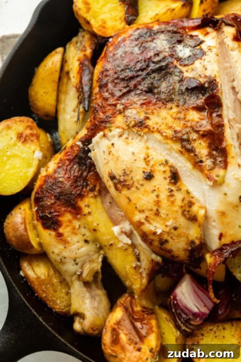 Garlic Butter Roasted Chicken and Crispy Potatoes 5 A whole roasted chicken in a cast iron skillet with a slice cut to reveal juicy meat. It is surrounded by golden, crispy potatoes.