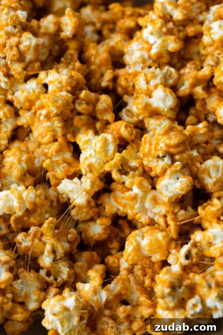 Cozy Fall Snack: Pumpkin Marshmallow Popcorn 3 Close-up of golden popcorn generously coated in vibrant, gooey pumpkin spice marshmallows, showcasing its irresistible texture.